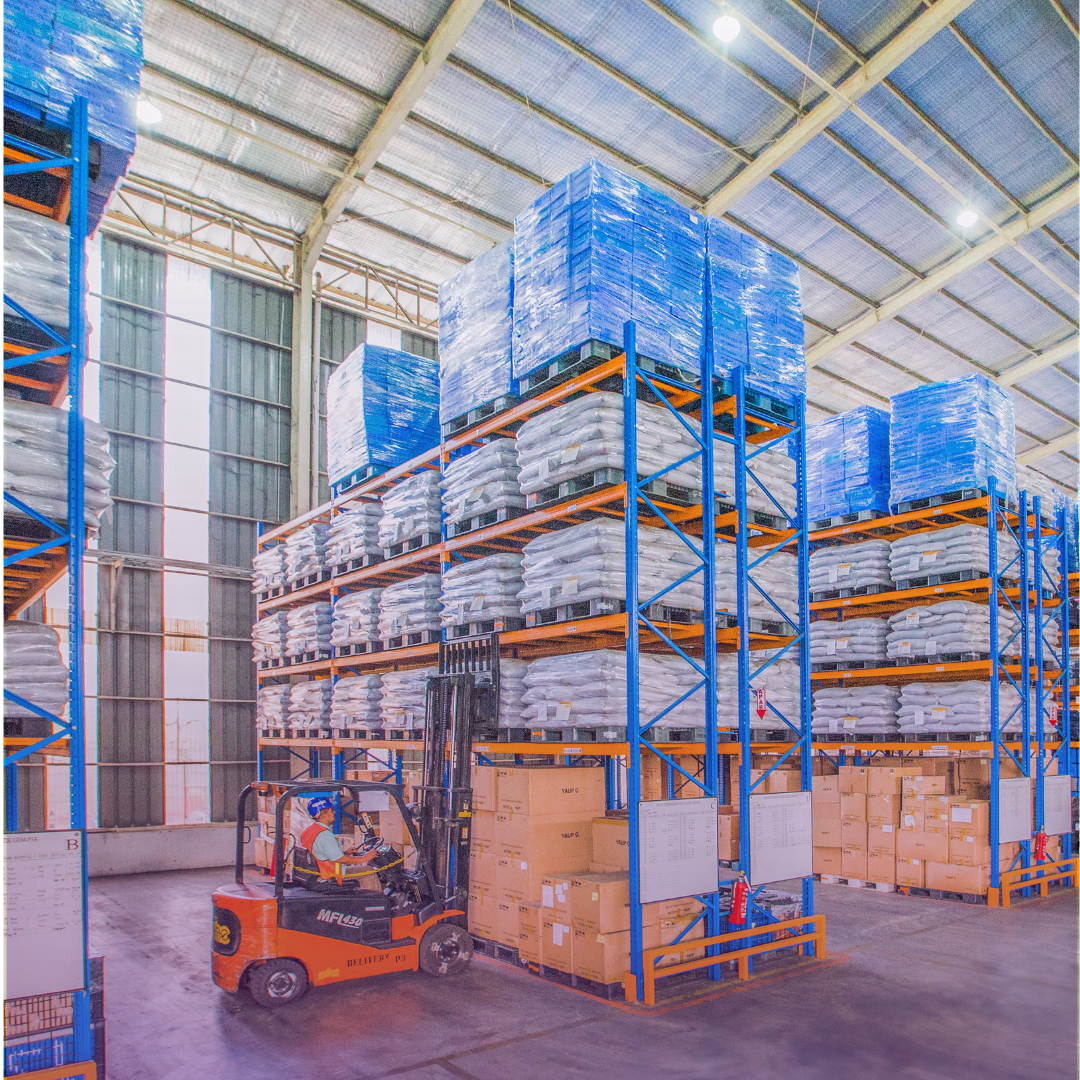 Expansive, organized warehouse with tall shelves, stacked goods, and an operating forklift, reflecting efficient distribution.