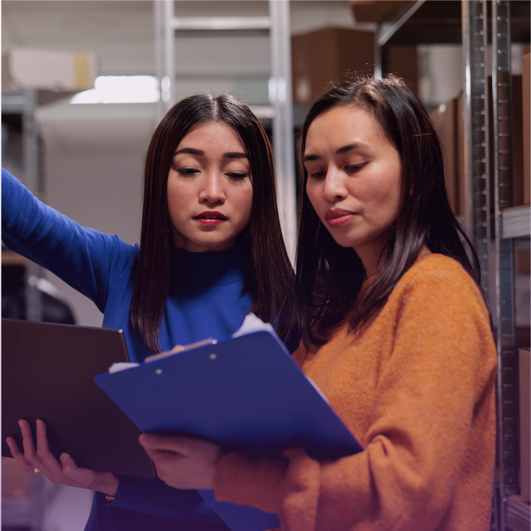 Two female warehouse professionals perform an inventory check, one reviewing a clipboard, symbolizing supply chain transparency and meticulous oversight.