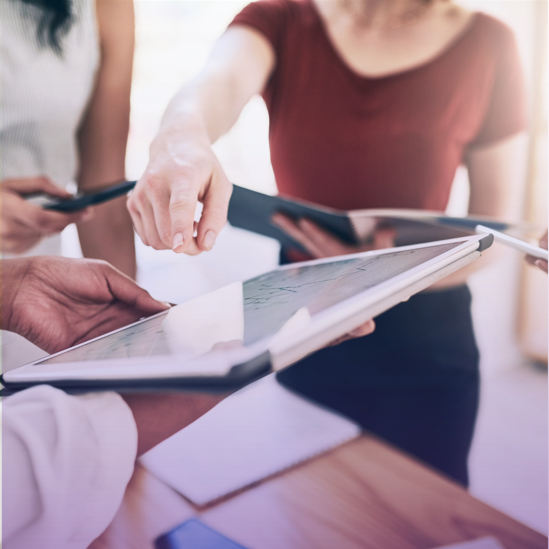 Under "Our Future Goals": A close-up view of three professionals actively collaborating around a tablet and notebook, with one hand pointing at the screen, symbolizing strategic planning, innovation, and teamwork towards future objectives.