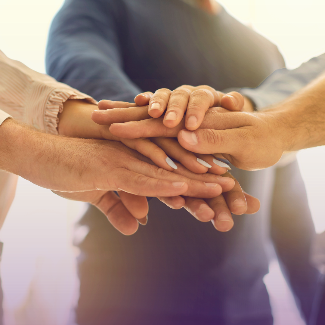 Close-up, low-angle shot of multiple diverse hands stacked tightly on top of each other, symbolizing teamwork, unity, and collaboration among a group.