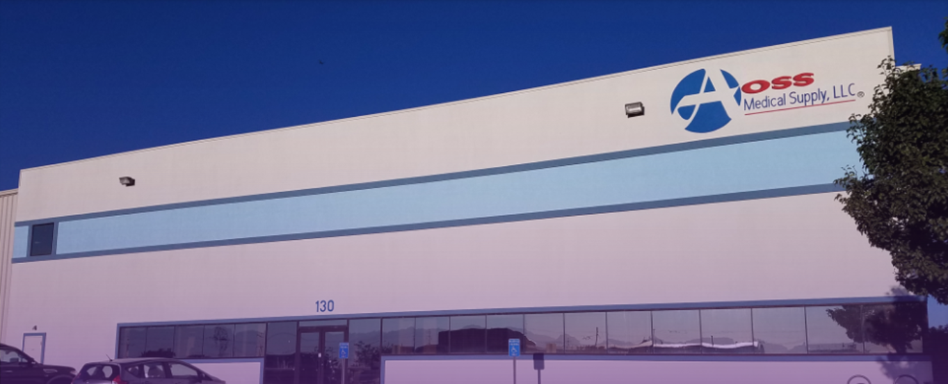 Exterior view of the AOSS Medical Supply, LLC. industrial building, featuring its blue logo on the white facade, blue horizontal window bands, and the building number 130.