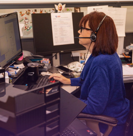 Under "OUR CORE MISSION & VALUES": A dedicated female customer service representative with reddish-brown hair, wearing glasses and a headset, intently working at a computer in an office cubicle, symbolizing a commitment to customer satisfaction and operational excellence.