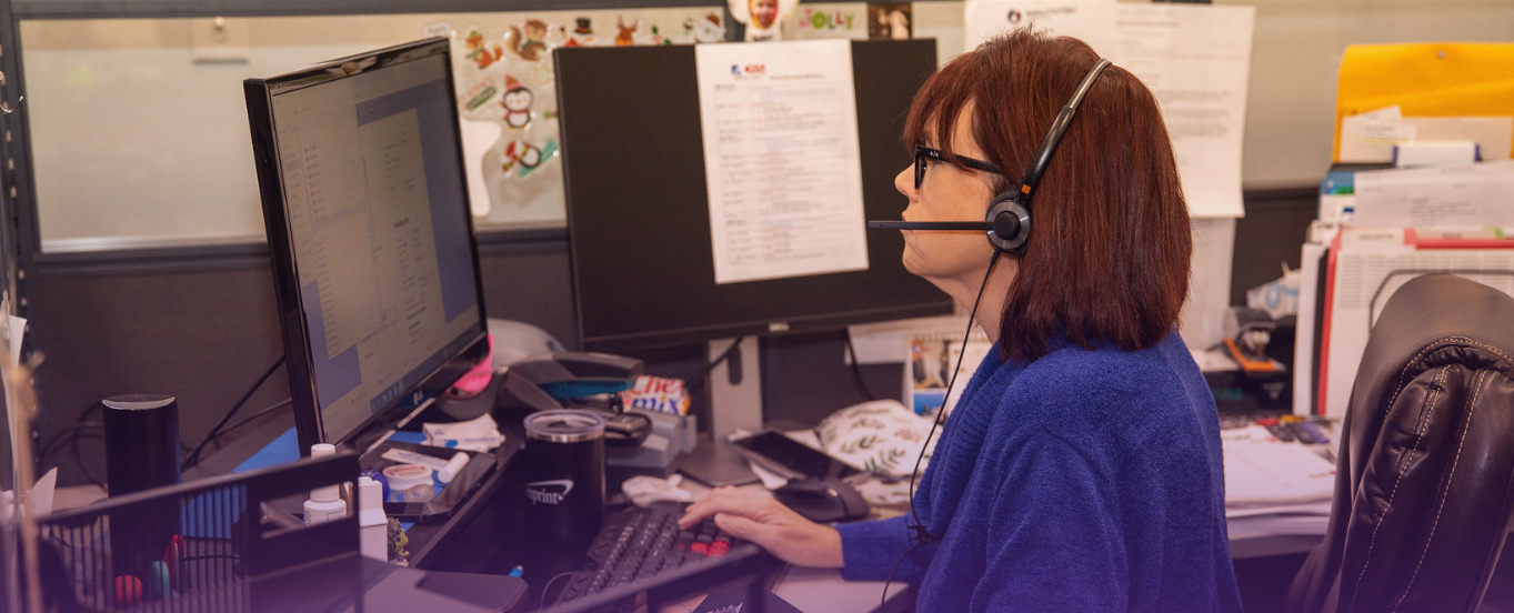Female customer service representative with headset types on computer, ready to assist.